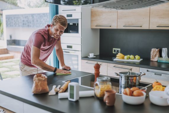 fröhlicher Mann putzt seine Küche nach dem Kochen