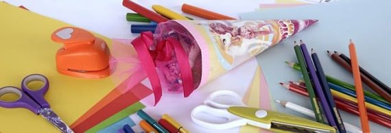 Eine selbstgebastelte Schultüte liegt zwischen stiften scheren und Buntem Papier auf einem tisch